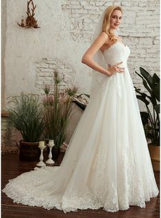 a woman wearing a wedding dress standing in front of a brick wall with potted plants