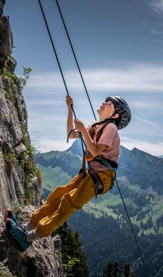 a man climbing up the side of a mountain with his helmet on and ropes attached to him