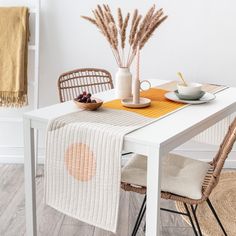 a white table topped with a bowl of fruit next to a vase filled with dry grass