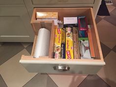 an open drawer with various items in it on the floor next to a counter top