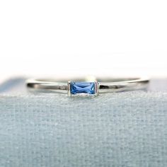 a white gold ring with a blue topazte stone set in the center, on a light blue cloth