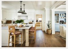 a large kitchen with white cabinets and wooden floors is pictured in this image, there are two bar stools at the center of the island