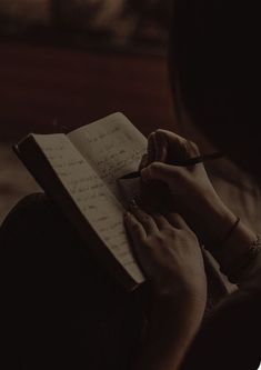 a woman is writing on a notebook in the dark with her hand holding a pen