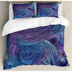 a bed covered in purple and blue comforters with an intricate design on the cover