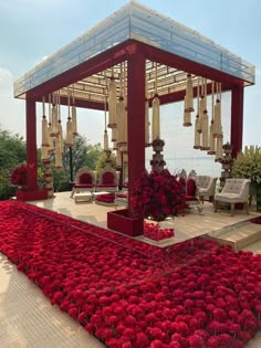 a gazebo with red flowers on the ground in front of it and an open area for seating