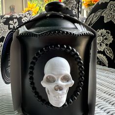 a white skull in a black box on a table with flowers and pillows behind it