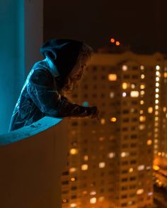 a young child standing on top of a building at night with city lights in the background