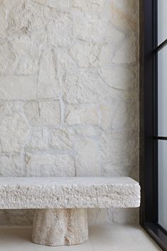 a stone bench sitting in front of a window next to a white brick wall and floor