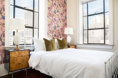 a bedroom with floral wallpaper and white bedding, two lamps on either side of the bed