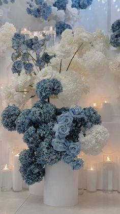 blue and white flowers are in a vase on the floor next to many lit candles