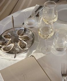 an empty plate with oysters on it next to wine glasses and utensils