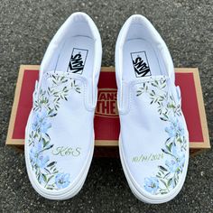 These White Slip On Vans have a soft flower design with gorgeous light blue flower arrangements and lush light green accents.  These are the perfect and comfortable gift for wearing on the big day while also enjoying them after the fact while out for brunch and reminiscing on saying "I Do".   Add a custom date and initials! The perfect shoes to get personalized. We buy each pair of blank shoes BRAND NEW directly from Vans. The ink is permanent and will never come off. Made in the USA. This price Spring White Slip-on Wedding Shoes, White Wedding Sneakers For Summer, Teal Wedding Shoes, Wedding Crocs, Custom Slip On Vans, Shoes Artwork, Sneakers Wedding, Wedding Shoes Sneakers, Blue Flower Arrangements