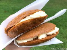 two sandwich halves with cream on them in paper wrappers, sitting on the grass