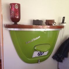 a green wall mounted urinal sitting on top of a white wall next to a wooden shelf