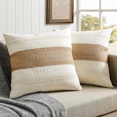 two pillows sitting on top of a couch next to a window with a framed picture above it