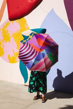 a woman standing in front of a colorful wall holding an open umbrella over her head