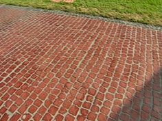 a red and white fire hydrant sitting on the side of a brick road next to a lush green field