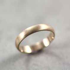 a gold wedding ring on a gray surface with no one in the photo looking at it