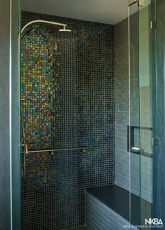 a glass shower door in a bathroom with blue and green mosaic tiles on the wall