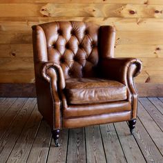 a brown leather chair sitting on top of a hard wood floor next to a wooden wall