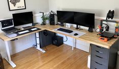 a desk with two computer monitors and a laptop on it, in front of a white wall