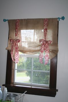 a kitchen window with curtains hanging from it's valance, and a basket in front of the window