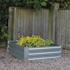 a large metal planter sitting on top of gravel next to a wooden fence and shrubbery