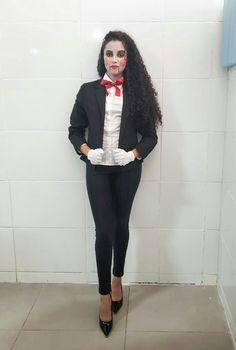 a woman dressed up as a clown standing in front of a white wall with her hands on her hips