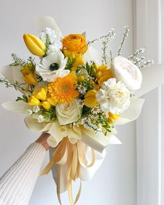 a bouquet of yellow and white flowers in someone's hand