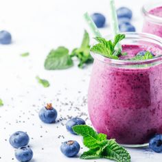 two mason jars filled with blueberry smoothie and mint sprigs on the side