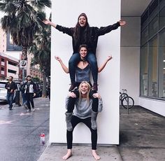 three people standing on top of each other in front of a building