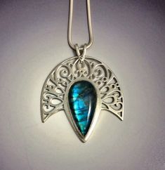 "The deep blue flash on this Labradorite was so glorious that it needed a halo. Enter a sheet of sterling silver and a jeweller's saw and we made the halo a reality. This gem's setting has been handcrafted with meticulous care - each tiny cutout is accomplished with precision and all corners and edges have been filed and polished until they shine with glory!  The pendant measures 41 X 45mm (approximately 1 3/4\" X 1 3/4\"). The chain is a snake style Italian Silver and measures 18\"." Celestial Silver Labradorite Jewelry, Handmade Mystical Blue Jewelry, Mystical Teardrop Sterling Silver Jewelry, Blue Mystical Pendant Jewelry, Mystical Blue Pendant Jewelry, Mystical Blue Labradorite Jewelry, Silver Labradorite Jewelry For Wedding, Unique Sapphire Sterling Silver Jewelry, Handmade Celestial Sapphire Jewelry