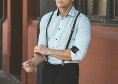 a man wearing suspenders and a white shirt is standing in front of a building