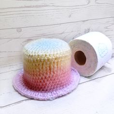 a crocheted hat and roll of toilet paper on a white wooden background with planks