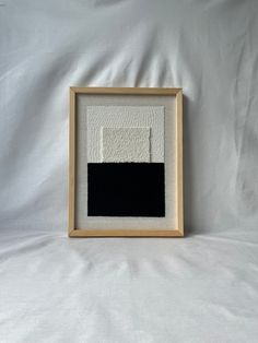 a black and white painting is displayed in a wooden frame on a white sheet background