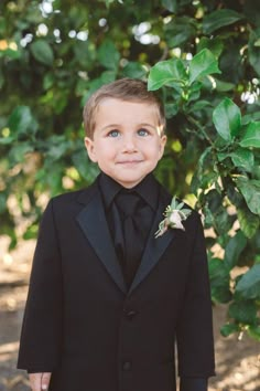 a young boy in a tuxedo smiles at the camera while wearing a boutonniere