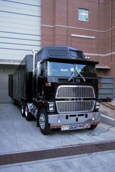 a black semi truck parked in front of a building with an overhead garage door open