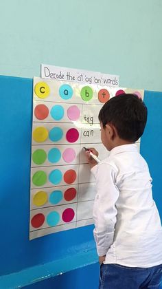 a young boy writing on a bulletin board with colorful circles and words written on it