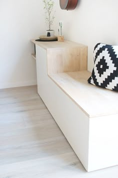 a white bench with a black and white pillow sitting on top of it next to a clock