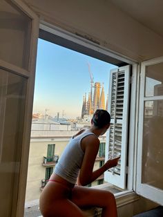 a woman sitting on a window sill looking out at the city