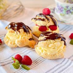 small pastries with chocolate drizzle and raspberries on a tablecloth