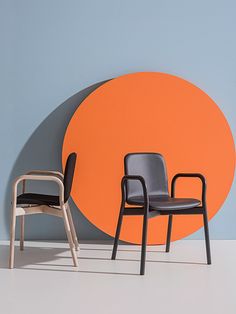 two chairs sitting next to each other in front of an orange and grey wall with a circular design on it