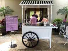 a small white cart with flowers on it and people in the background at an outdoor event