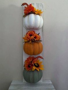 three pumpkins are stacked on top of each other in front of a white wall