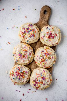 sprinkled cookies on a cutting board with white frosting and multicolored sprinkles