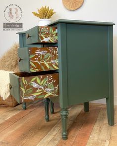 a green dresser with drawers painted with flowers and leaves on the front, sitting on a wooden floor next to a wall