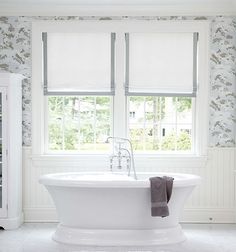 a white bath tub sitting next to two windows in a room with wall paper on the walls