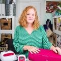 a woman sitting at a desk with a pink suitcase in front of her and several other items on the table