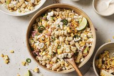 a bowl filled with corn salad next to two bowls full of other food on the table