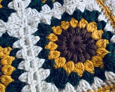 a crocheted sunflower is shown on top of a white blanket with green, yellow and brown accents